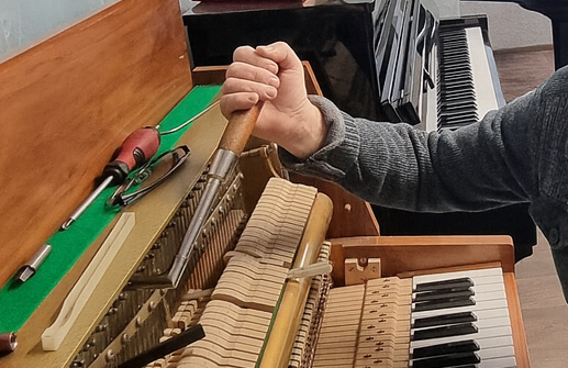 Hand stimmt Klavier und hält Stimmschlüssel